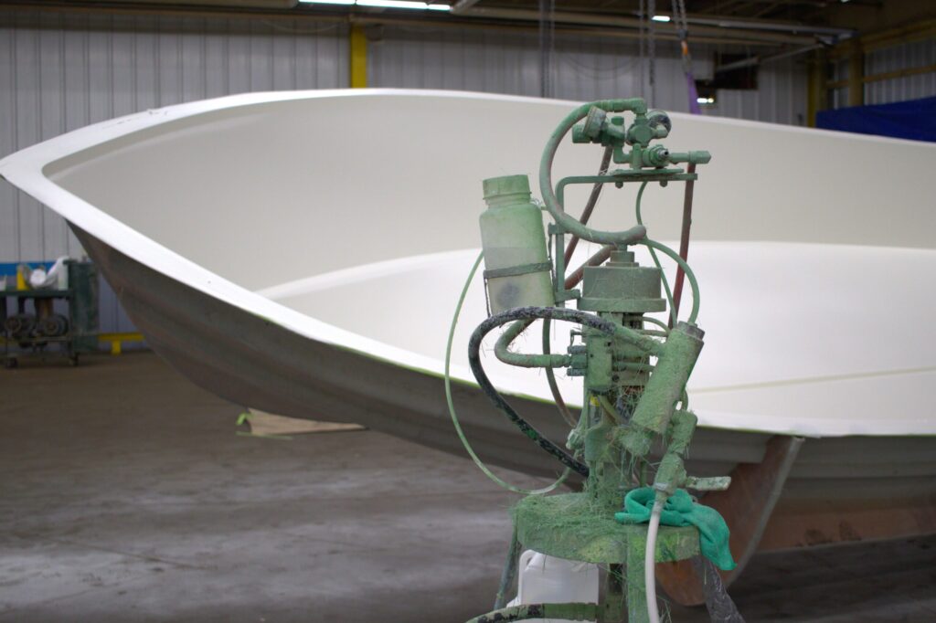 Gelcoat machine stands in front of a boat in a mold